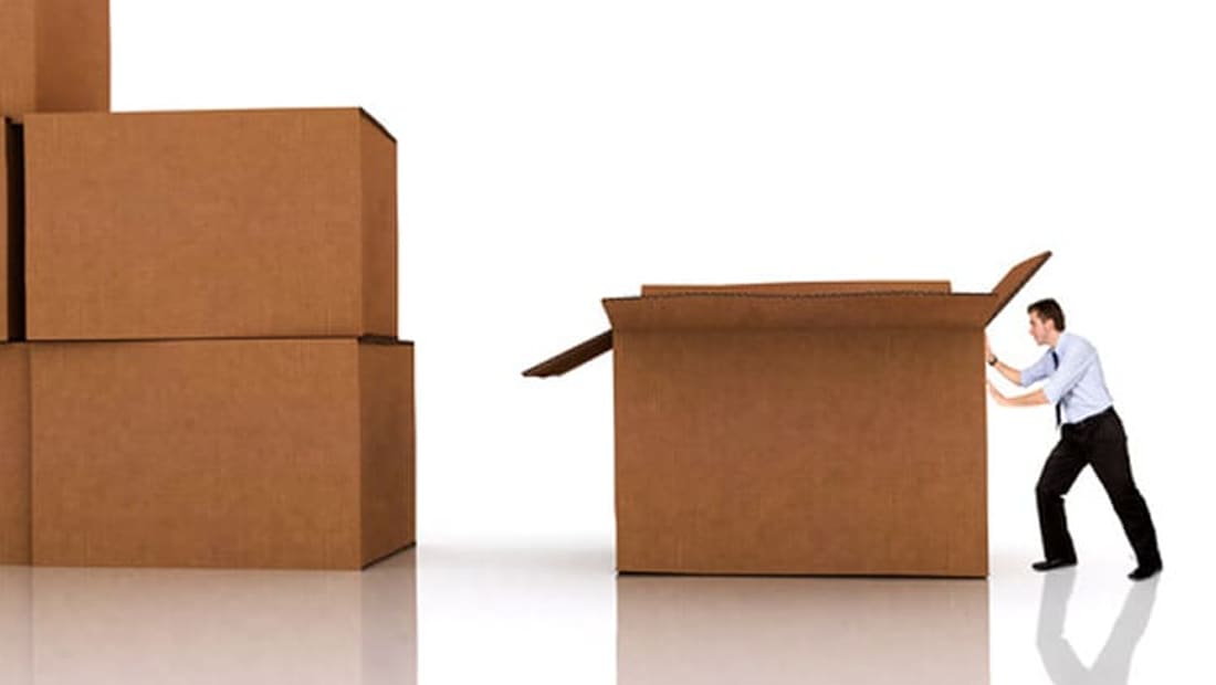 Man closing up a large cardboard box next to a stack of packed boxes